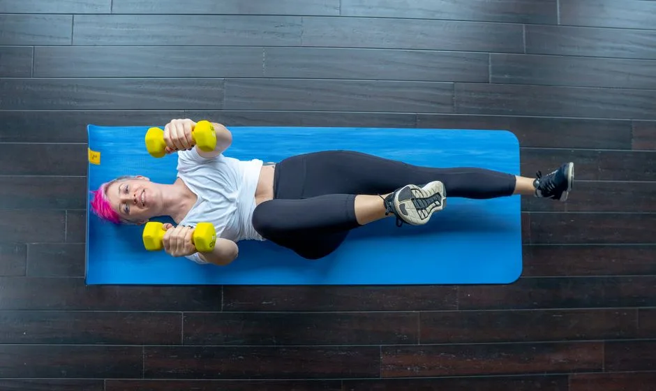 A woman working out with dumbbells on a yoga mat in a gym setting indoors.