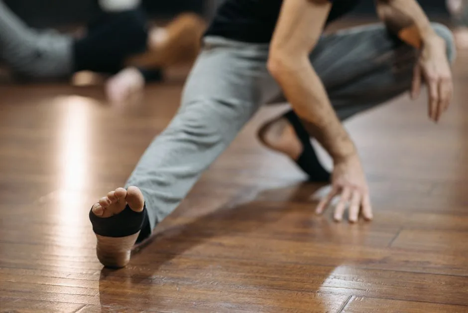Close shot of man stretching on wooden floor, focusing on foot and hand positioning.