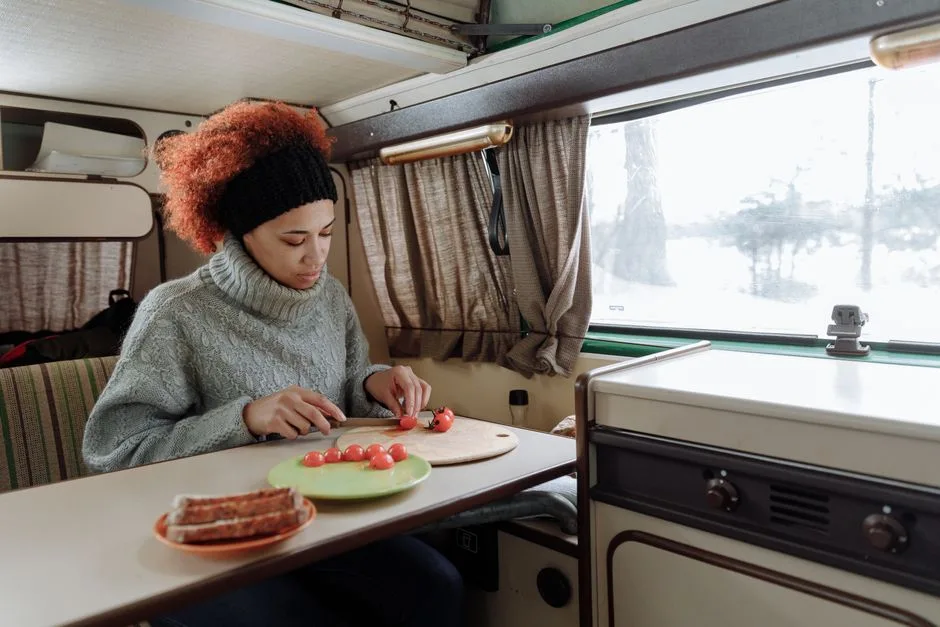 A woman chops cherry tomatoes in a camper van kitchen, showcasing a cozy van life scene.