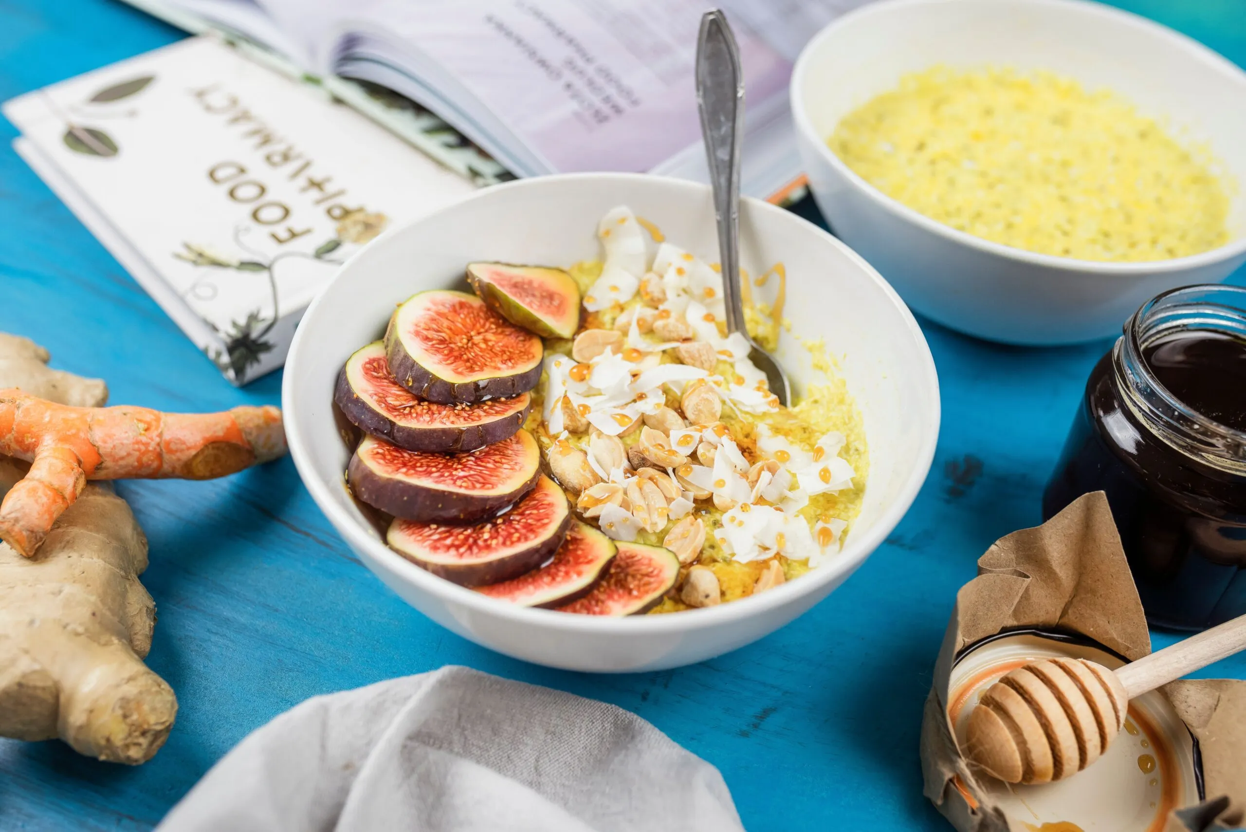 Healthy breakfast bowl with figs, nuts, and turmeric on a blue table with ginger and honey.