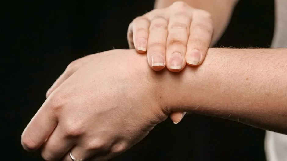 Close-up of a person's hands pressing their wrist, focusing on skin and texture.