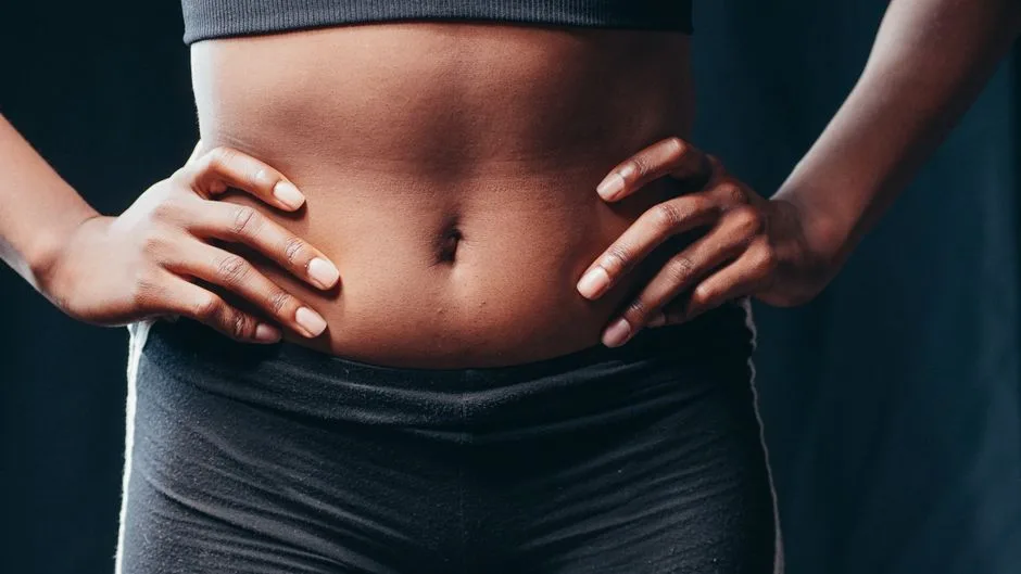 A close-up of a woman's toned midsection with hands on hips, showcasing fitness and health.