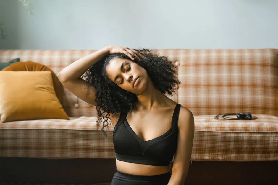 Woman with curly hair practicing neck stretches indoors, embodying a healthy lifestyle.