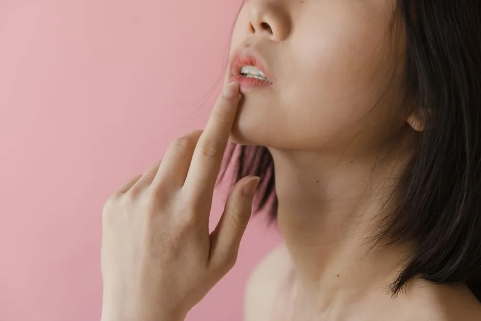 Close-up portrait of a woman gently touching her lip against a pink backdrop.