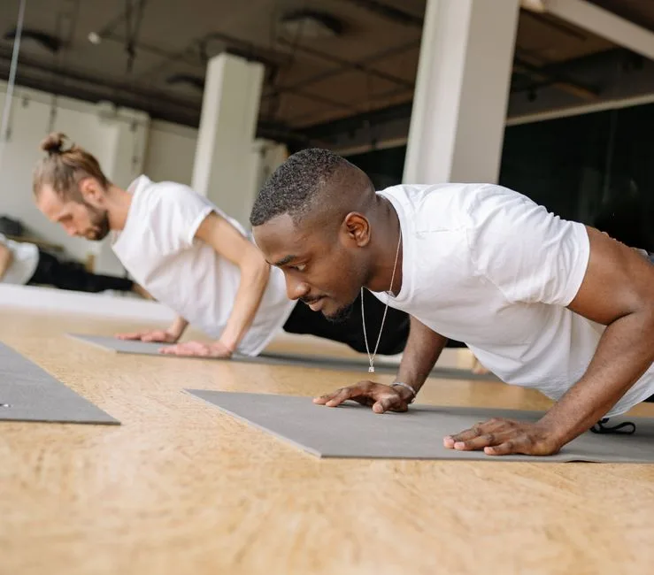 Two adult men working out indoors, focusing on push-ups for strength training.