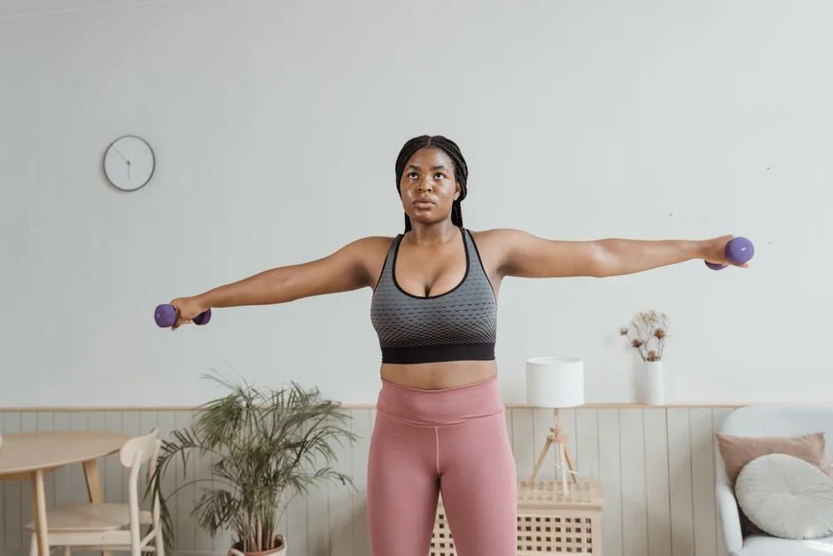 Black woman in activewear performing arm exercises indoors with dumbbells.