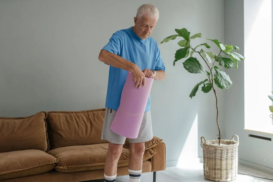 Elderly man in cozy room rolling out yoga mat for a healthy lifestyle workout.