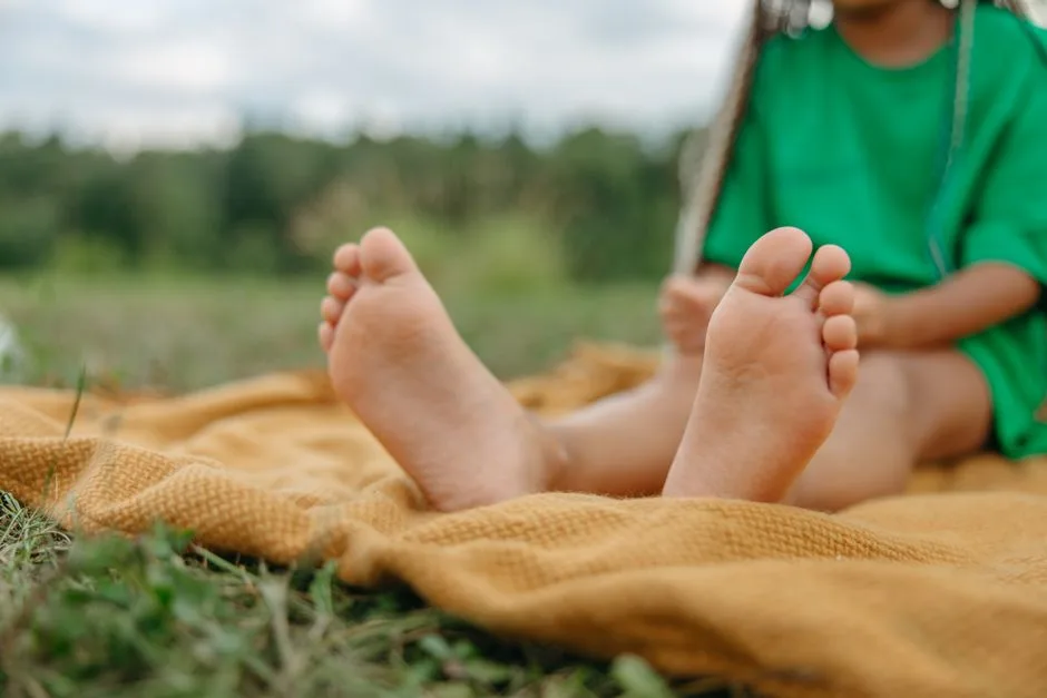 Close-up of a child's feet on a picnic blanket outdoors, enjoying a sunny day.