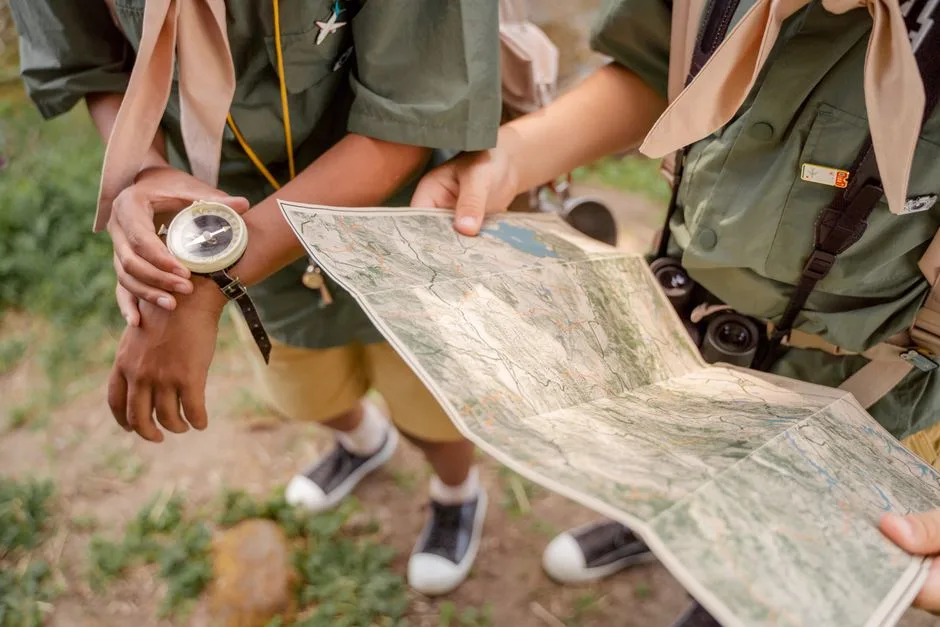 Two scouts examining a map with compass in hand, capturing the essence of navigation outdoors.