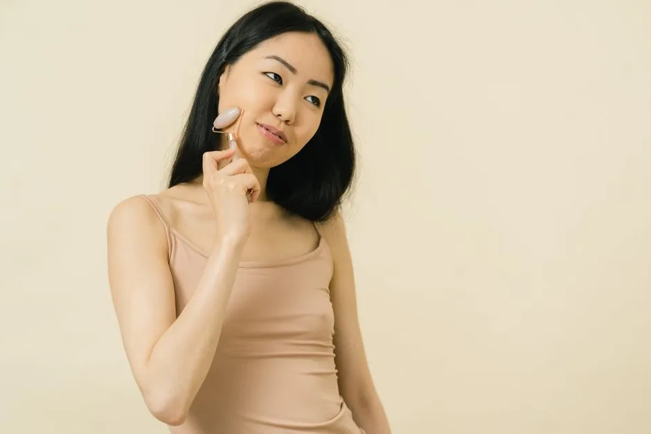 Asian woman using a gua sha roller for facial skincare in a studio setting.