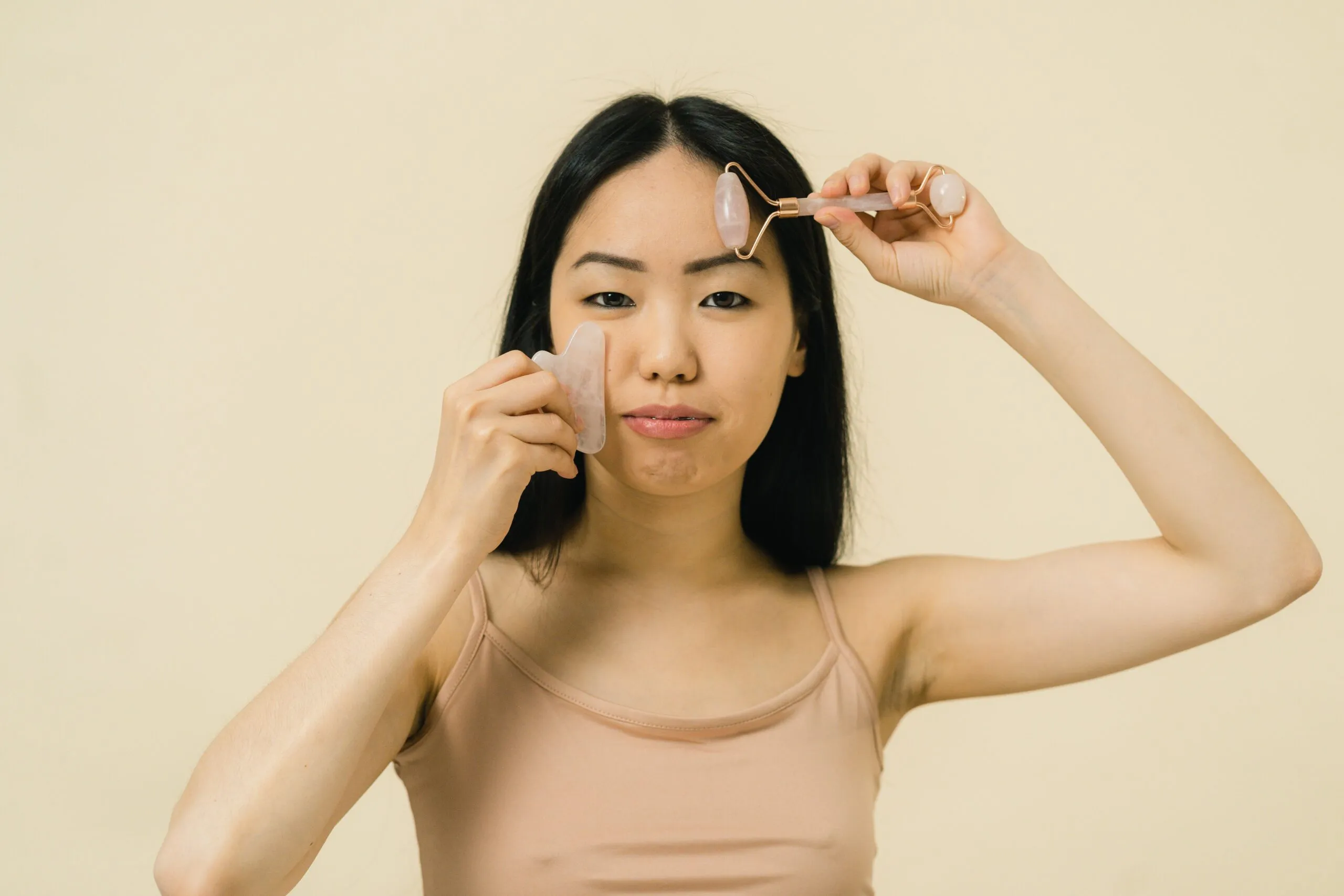 Asian woman using a facial roller for skincare and self-care in a studio setting.