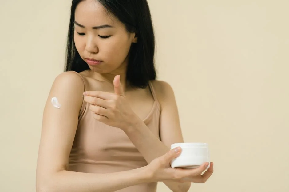 A woman applies moisturizing cream on her arm, focusing on skincare and self-care.