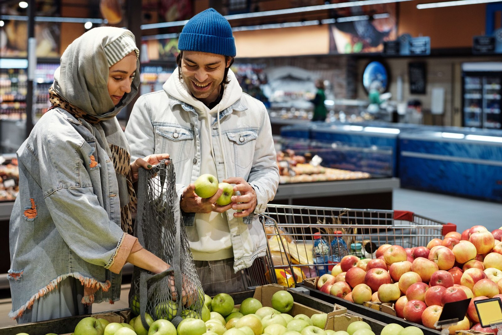 A smiling couple selects apples together in a vibrant supermarket setting.