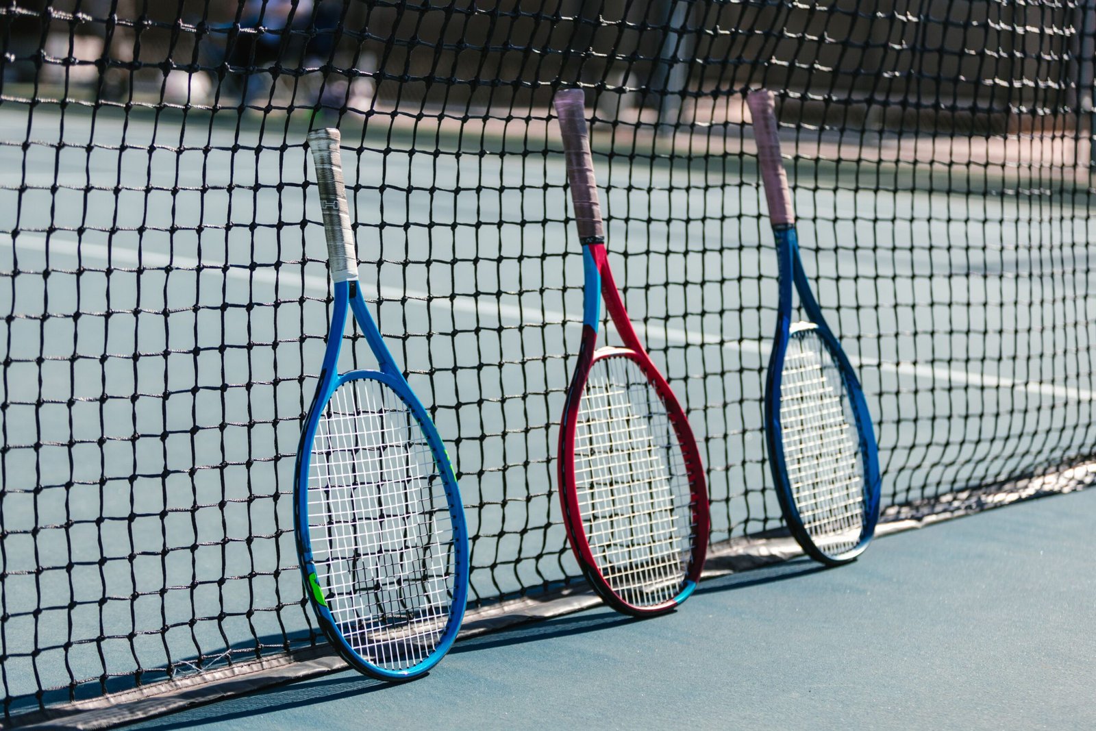 Three colorful tennis rackets leaning against a net on an outdoor tennis court.
