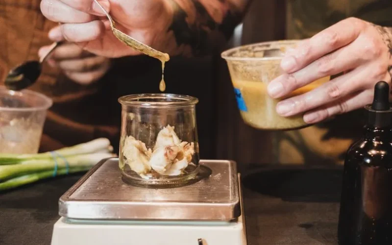 Close-up of chef measuring ingredients in a glass jar on a kitchen scale.