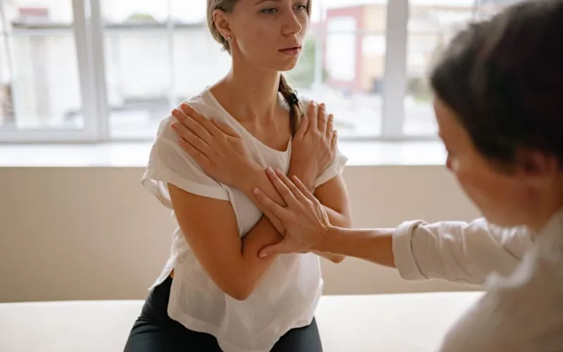 Therapist guiding a woman in a stretching exercise indoors, focusing on physical therapy.