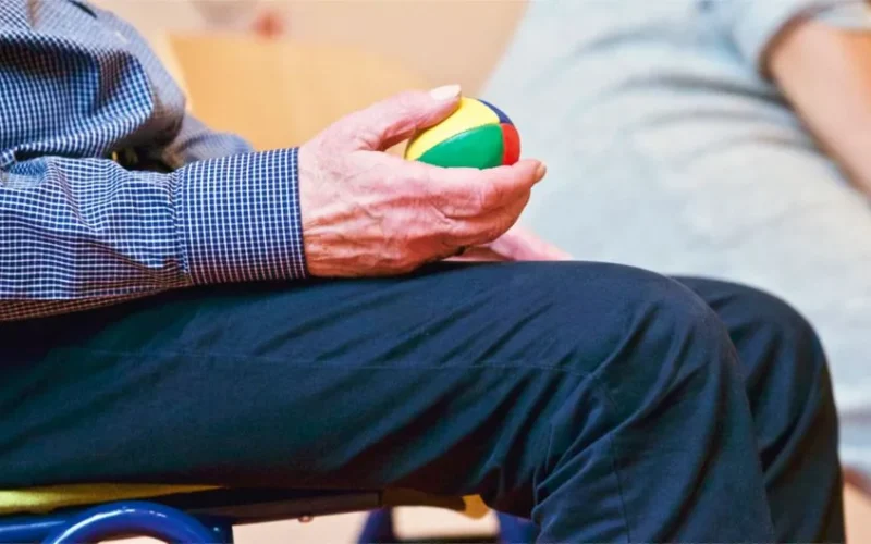 Elderly man holding a colorful therapy ball indoors, promoting relaxation and health.