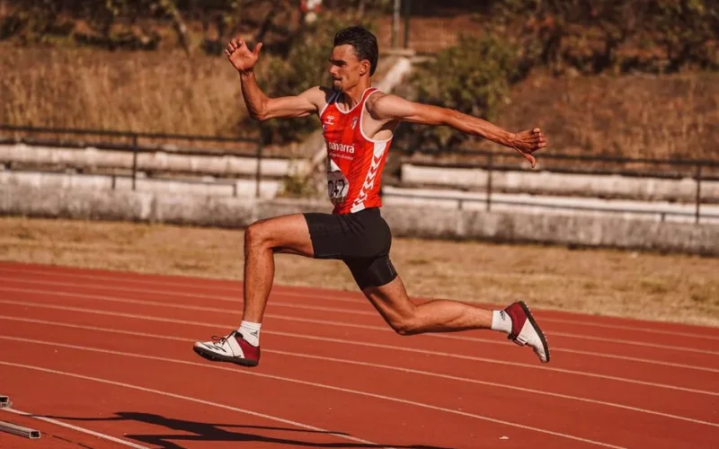 Energetic athlete captured mid-jump during a track event, showcasing strength and agility.