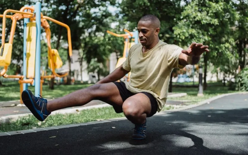A man performing a balance exercise in an outdoor park with fitness equipment, emphasizing strength and wellness.