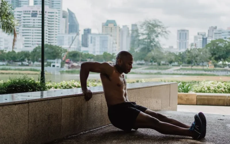 A fit man performs tricep dips in an urban park with a city skyline backdrop, embracing strength and wellness.