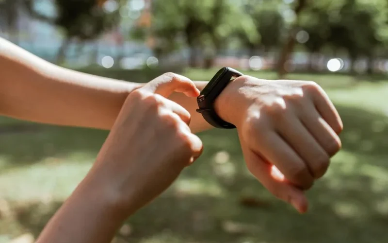 Crop faceless slim female tapping on fitness bracelet screen while training time in sunny summer park