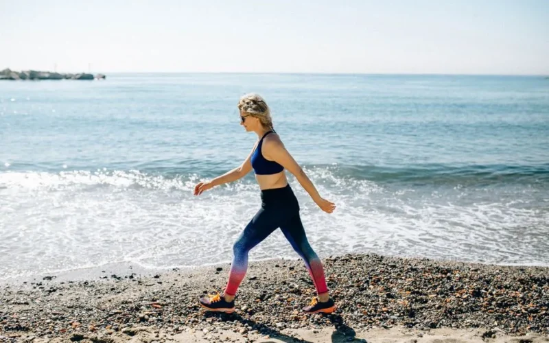A woman in activewear power walks along a sunny beach shore, enjoying the healthy lifestyle and ocean view.