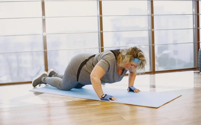 Adult woman doing push-ups indoors on a yoga mat, embracing a healthy lifestyle.