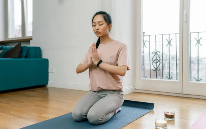 A woman practicing meditation and relaxation indoors on a yoga mat, promoting a healthy lifestyle.