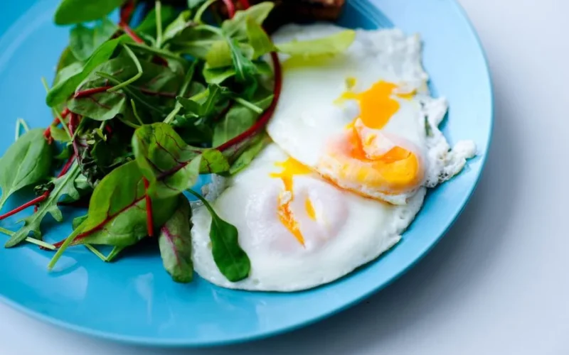A vibrant plate of poached eggs with fresh greens on a blue plate, perfect for breakfast.
