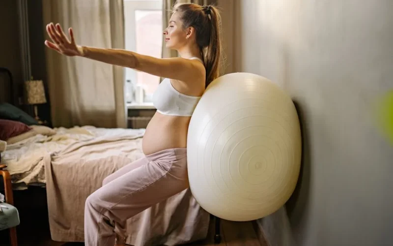 Pregnant woman practicing fitness exercises at home using a stability ball for healthy living.