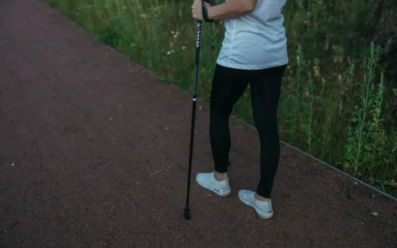A person in athletic wear uses a trekking pole while walking on a forest pathway.
