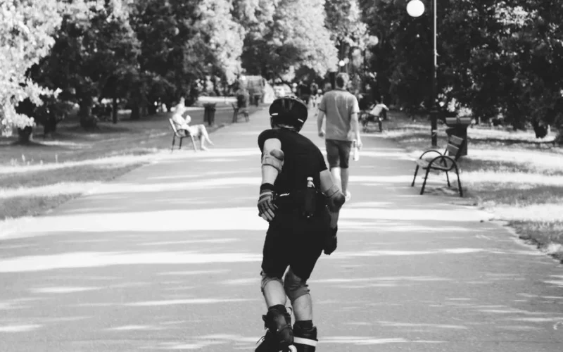 Black and white photo of a person rollerblading on a park path, captured in motion.