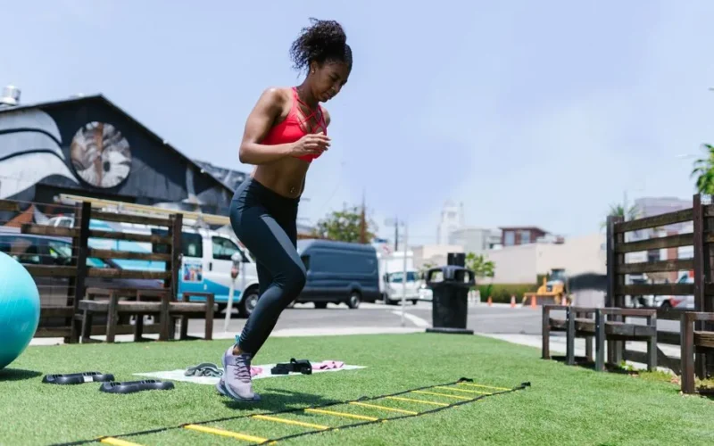 Black woman performing fitness exercises using agility ladder outdoors