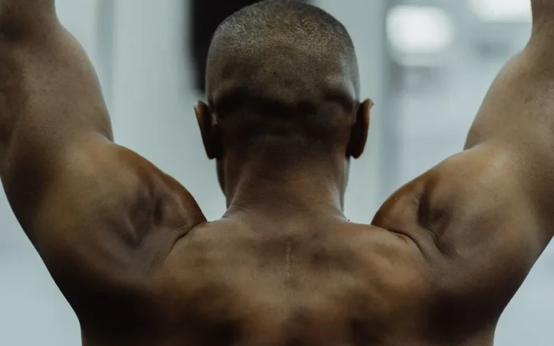 Shirtless man showing strength with visible muscles during workout, focus on back view.