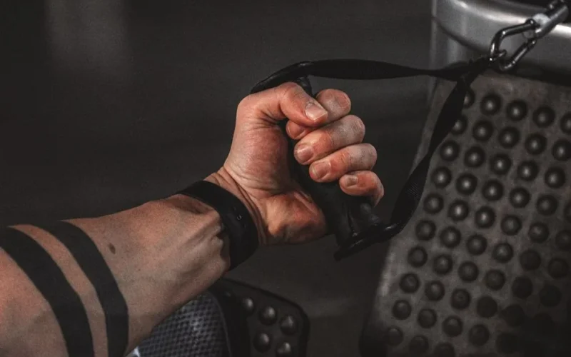 Close-up of a male hand gripping gym cable, showcasing strength and arm tattoo.