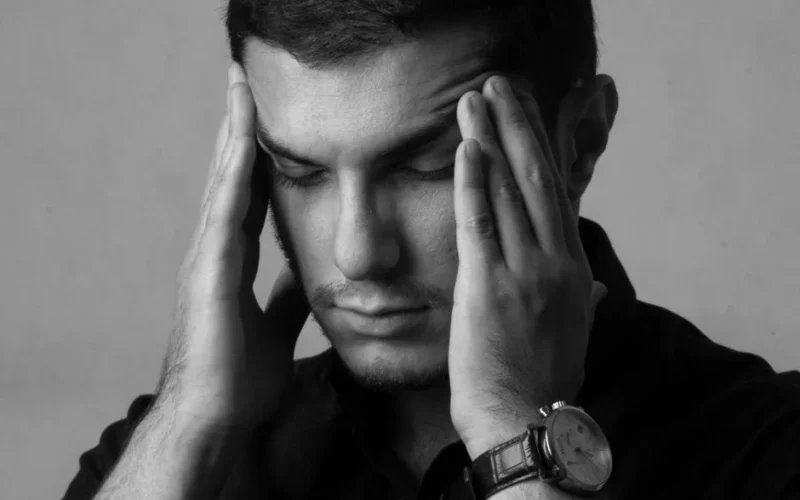 Close-up black and white portrait of a man holding head, indicating stress or headache.