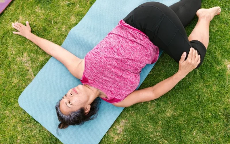 An adult woman performing a yoga stretch on a mat outdoors, promoting healthy lifestyle and fitness.