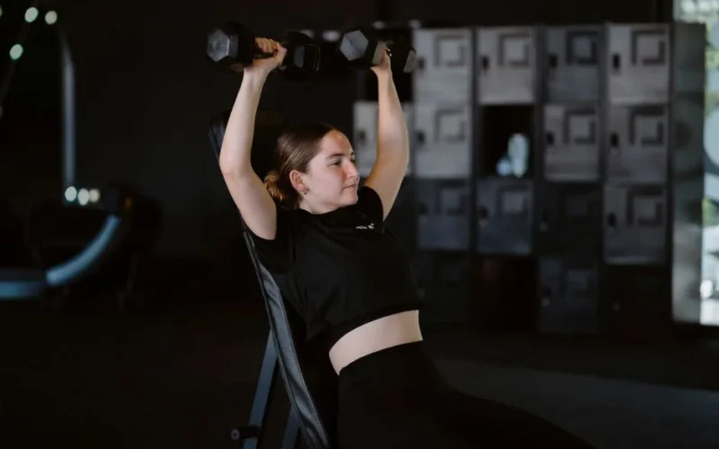 Young woman lifting dumbbells at gym showcasing strength training and fitness lifestyle.