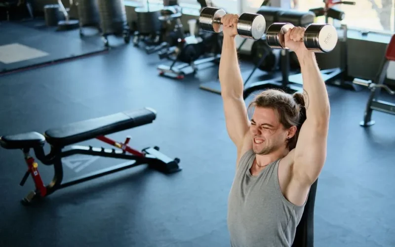 Man intensely lifting dumbbells in a modern gym, showcasing strength and endurance.