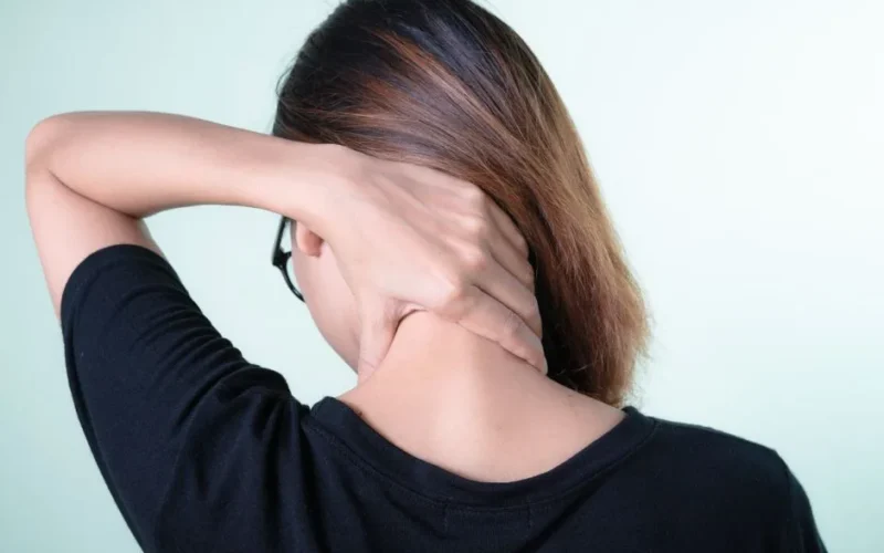 Rear view of a woman massaging her neck, depicting neck pain relief or self-care concepts.