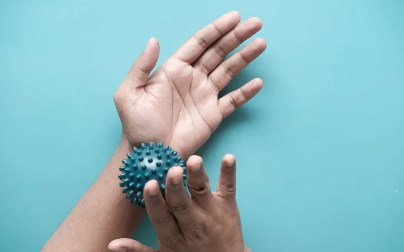Close-up of hands using a spiky massage ball for therapy against a blue backdrop.