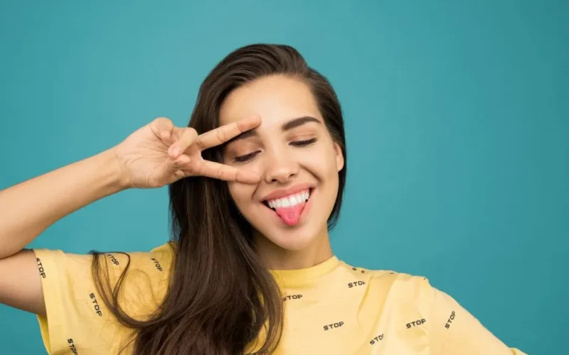 Cheerful young woman posing with a playful hand gesture and sticking her tongue out.