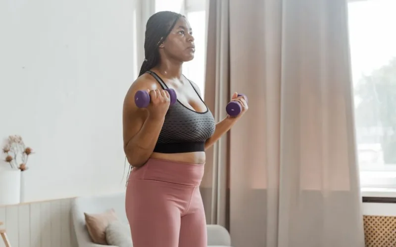 A plus size woman exercises indoors with dumbbells, promoting health and fitness.