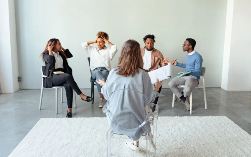 People engaging in a group therapy session indoors, discussing mental health topics.