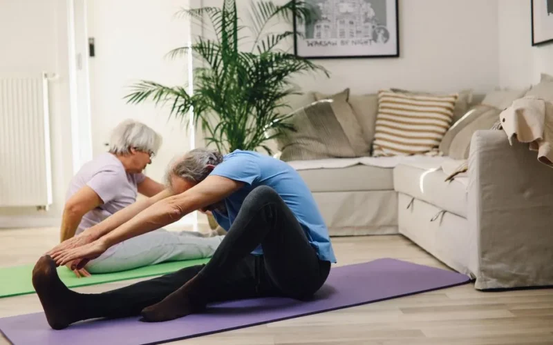 Two senior adults performing yoga stretches in a cozy living room setting.