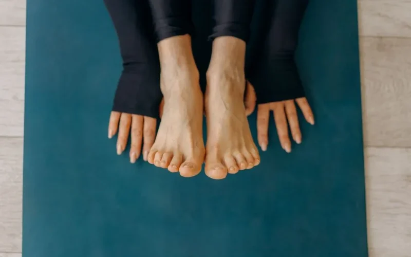 Close-up of feet and hands on a blue yoga mat in a calm indoor setting.