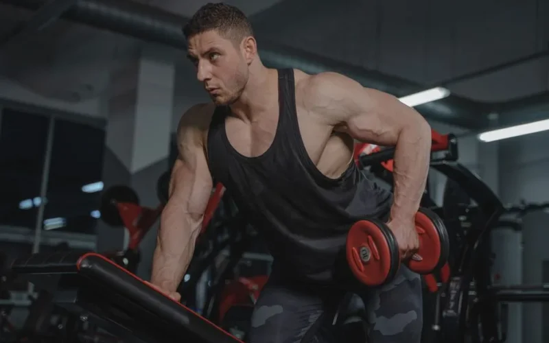 Strong male bodybuilder lifting dumbbells in a gym environment.