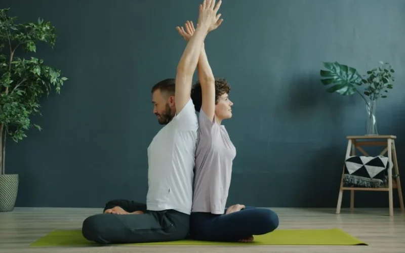 Two adults performing seated yoga poses on a mat indoors.