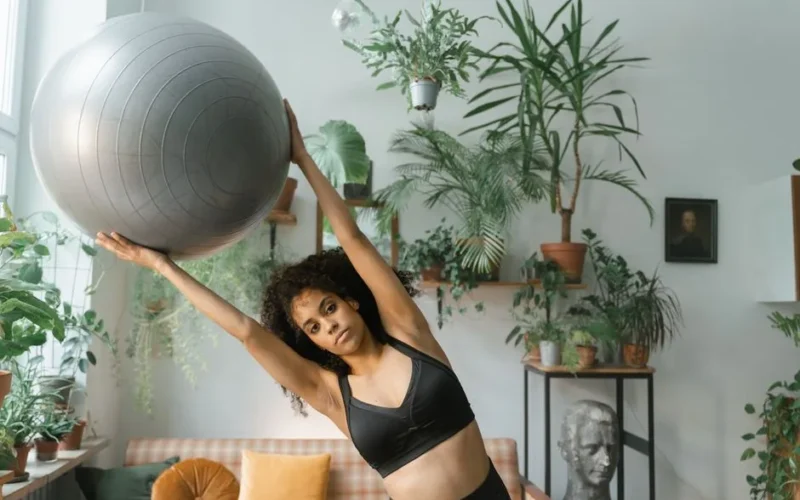 A woman exercises with a fitness ball surrounded by lush indoor plants, promoting a healthy lifestyle.