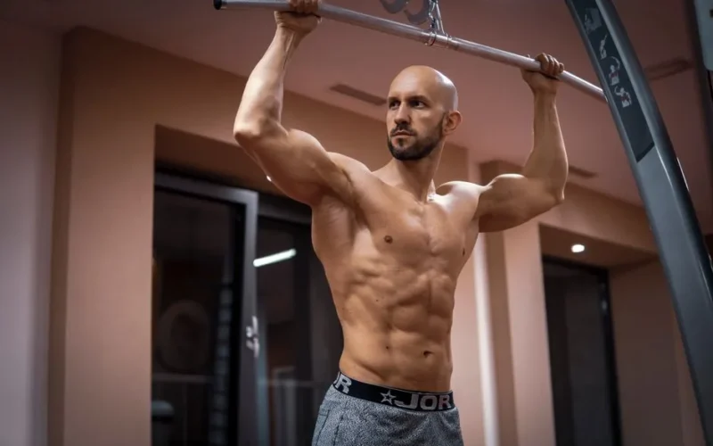 A bald, muscular man performing exercise on gym equipment indoors.